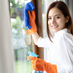 Asian woman wearing Protective Gloves Cleaning Window by spraying Cleaning Products